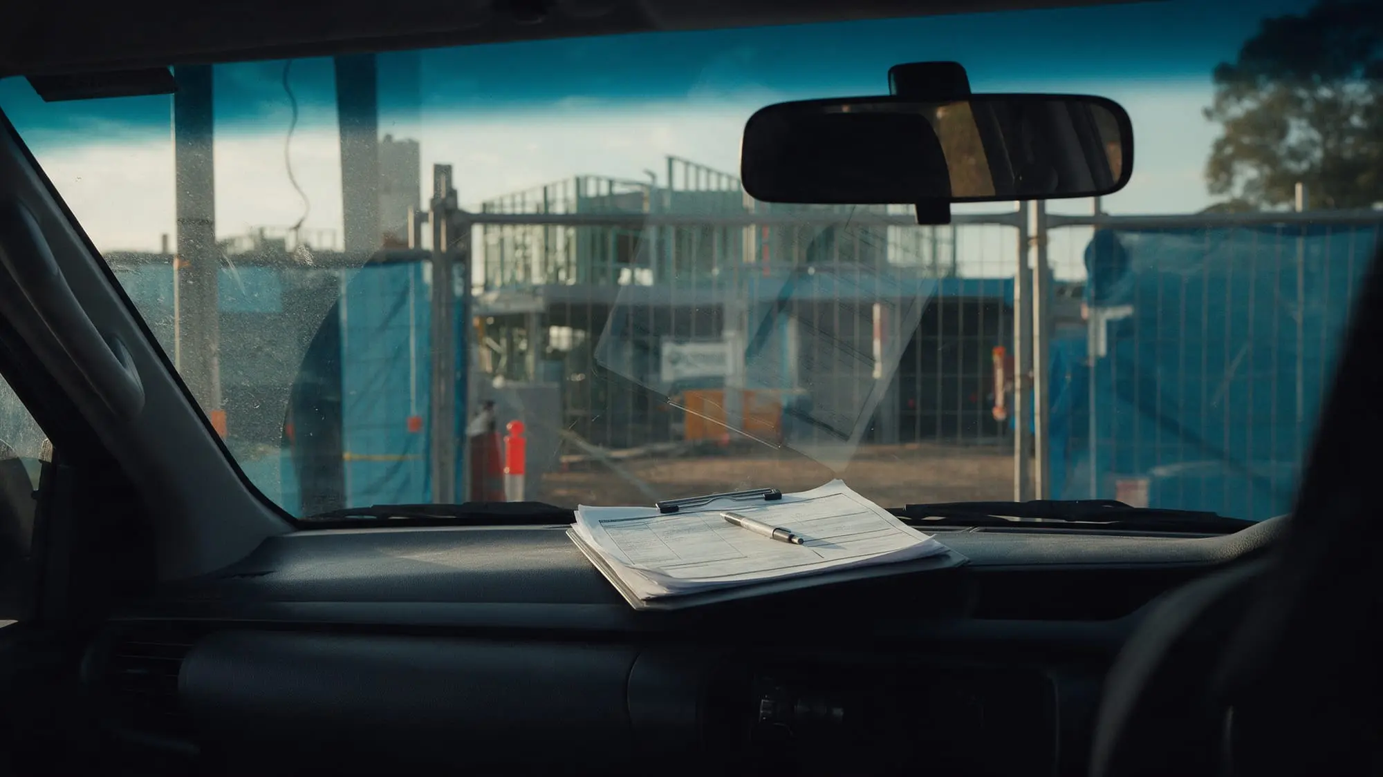 A clipboard of forms on the dashboard of a ute parked at a building site gate